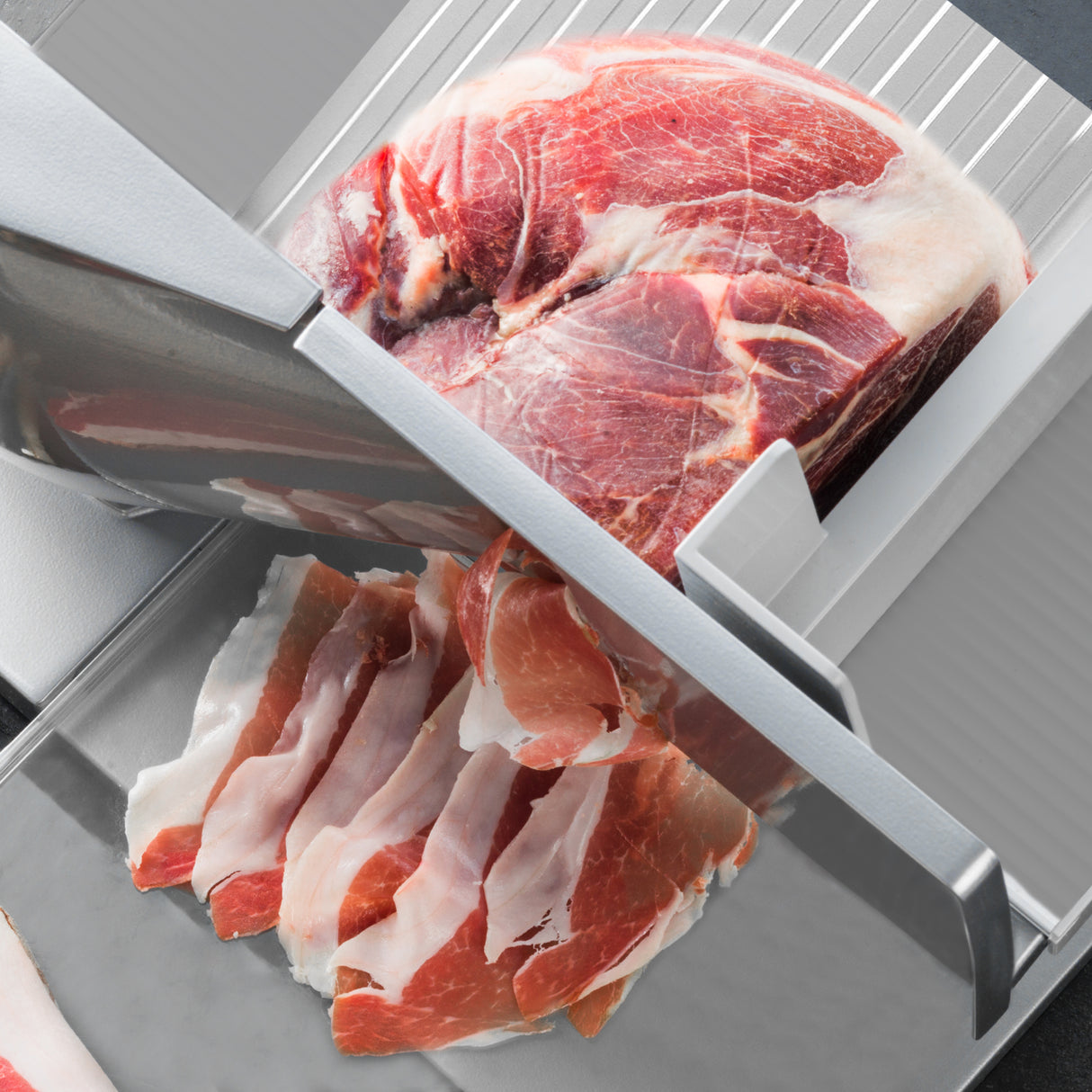 Trancheuse de viande KuKoo en acier inoxydable, avec un bloc de viande rouge et des tranches de jambon rose sur un fond gris