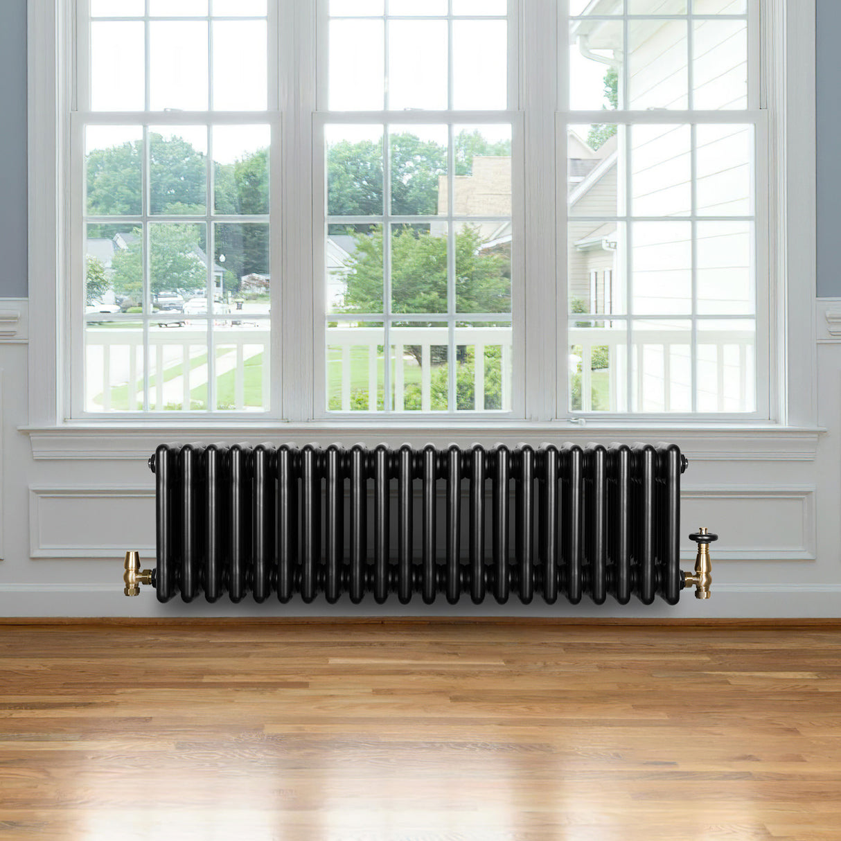 Radiateur traditionnel noir à 4 colonnes, 300 x 1010 mm, installé sous une fenêtre, avec des robinets en laiton et un sol en bois clair