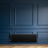 Radiateur traditionnel noir à 4 colonnes, 300 x 1010 mm, installé contre un mur bleu, avec des détails en laiton et un sol en bois clair