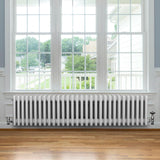 Radiateur traditionnel à 4 colonnes blanc, 300 x 1370 mm, installé sous une fenêtre, avec un sol en bois clair et un cadre moderne