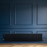 Radiateur traditionnel à 4 colonnes gris anthracite, installé contre un mur bleu, avec un sol en bois clair et des détails élégants