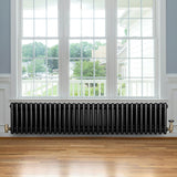 Radiateur traditionnel noir à 4 colonnes, 300 x 1505 mm, installé sous une fenêtre avec vue sur un jardin, sol en bois clair