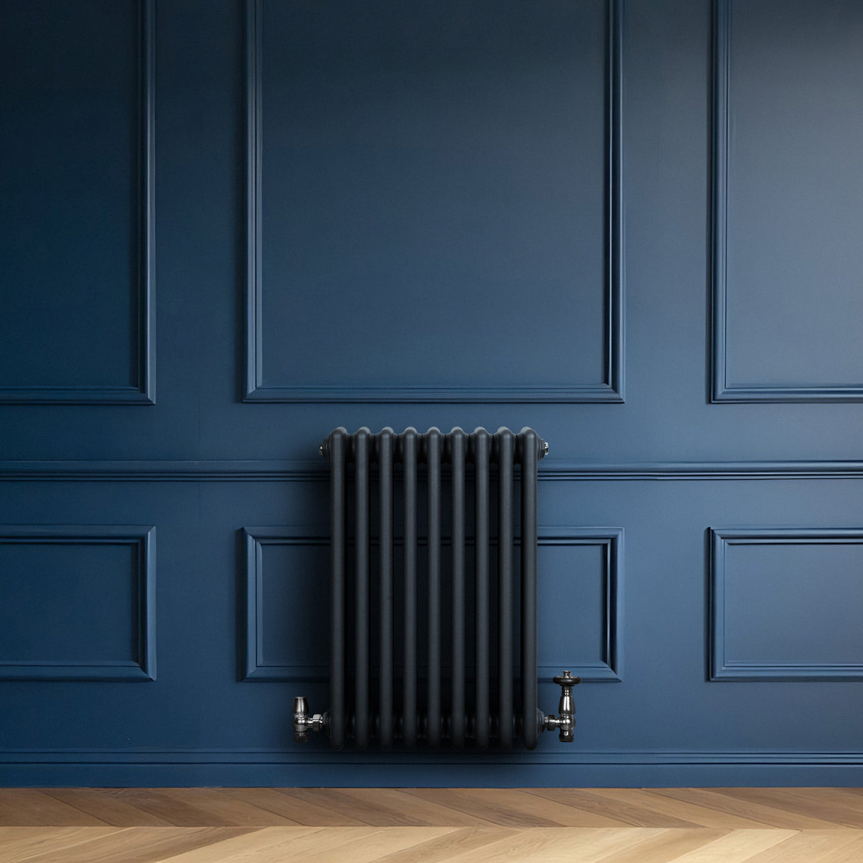 Radiateur traditionnel à 4 colonnes gris anthracite, installé sur un mur bleu, avec des tuyaux en métal et un sol en parquet clair