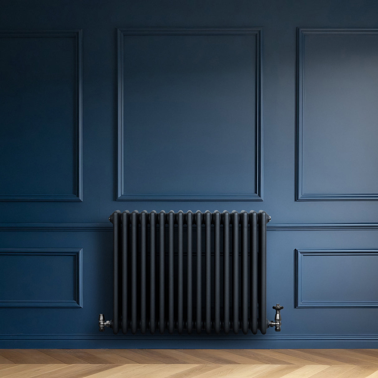 Radiateur traditionnel à 4 colonnes gris anthracite, installé sur un mur bleu, avec des détails en métal et une texture lisse