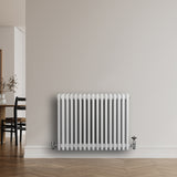 Radiateur traditionnel à 4 colonnes, blanc, finition lisse, installé sur un mur clair, avec un sol en bois et une ambiance moderne