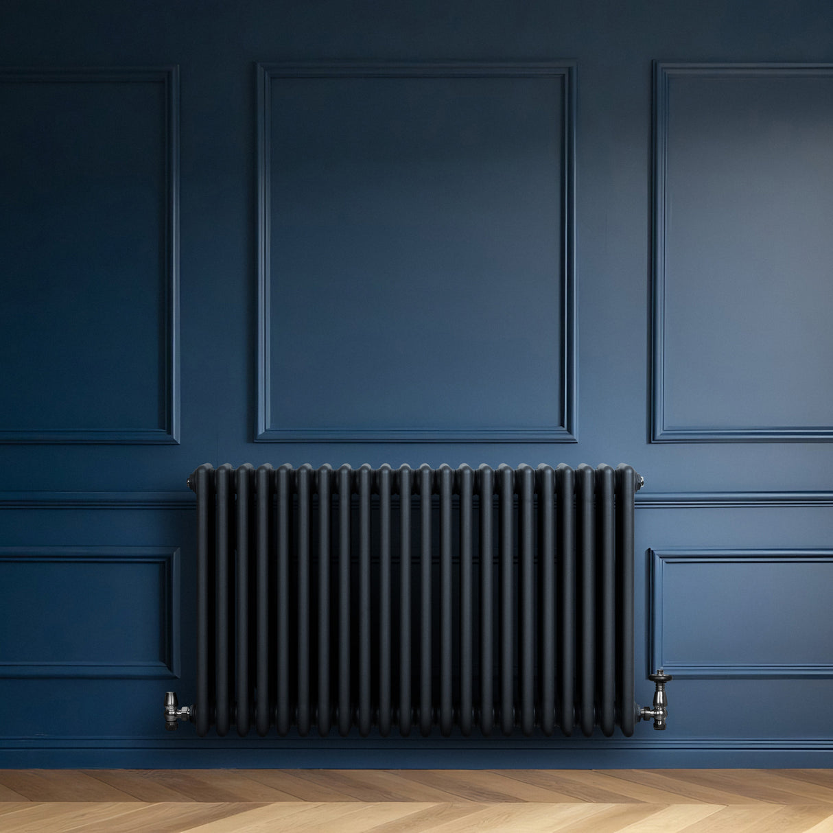 Radiateur traditionnel à 4 colonnes, gris anthracite, installé contre un mur bleu foncé, avec un sol en parquet clair
