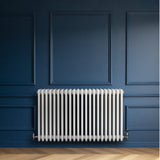 Radiateur traditionnel à 4 colonnes en blanc, installé sur un mur bleu, avec des lignes épurées et une finition lisse