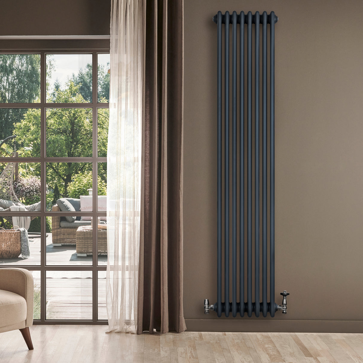 Radiateur traditionnel à 4 colonnes gris anthracite, haut et étroit, installé sur un mur beige, avec des fenêtres laissant entrer la lumière naturelle