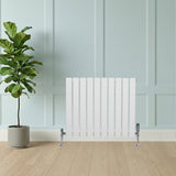 Radiateur plat blanc à un panneau, 600 x 700 mm, installé contre un mur clair, avec des pieds chromés et un sol en bois clair