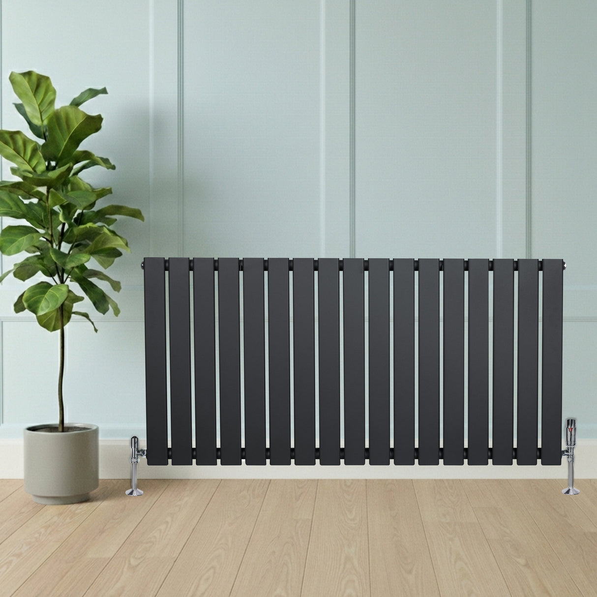 Radiateur plat gris anthracite à un panneau, installé au sol, avec des pieds chromés, devant un mur clair et une plante verte