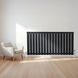 Radiateur plat noir à un panneau, 600 x 1190 mm, installé sur un mur clair, avec un sol en bois et un fauteuil moderne à côté