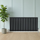 Radiateur plat noir à 1 panneau, 600 x 1190 mm, avec des lattes verticales et des pieds en métal, placé près d'une plante verte