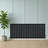 Radiateur plat noir à un panneau, 600 x 1400 mm, avec des lattes verticales, installé contre un mur, à côté d'une plante en pot