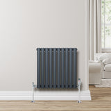 Radiateur à colonnes ovales gris anthracite, 600 x 600 mm, installé contre un mur clair, avec des pieds en métal chromé