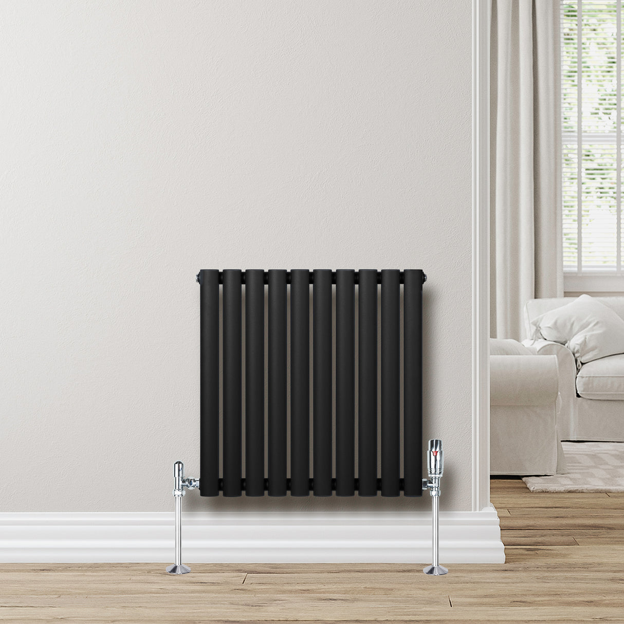 Radiateur à colonnes ovales noir, 600 x 600 mm, installé contre un mur clair avec des pieds chromés et un intérieur moderne lumineux