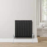 Radiateur à colonnes ovales noir, 600 x 600 mm, installé contre un mur clair avec des pieds chromés et un intérieur moderne lumineux