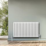 Radiateur à colonnes ovales blanc, 600 x 1020 mm, avec surface lisse et moderne, installé sur un mur gris, décoré de verdure extérieure
