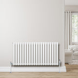Radiateur à colonnes ovales blanc, 600 x 1200 mm, installé contre un mur clair, avec des pieds chromés et un intérieur lumineux en arrière-plan