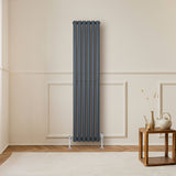 Radiateur à colonnes ovales gris anthracite, 1600 x 360 mm, installé sur un mur beige, avec un sol en bois et une table en bois clair à proximité