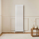 Radiateur à colonnes ovales blanc, 1600 x 480 mm, installé sur un mur beige, avec un sol en bois et une table en bois à proximité