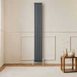 Radiateur à colonnes ovales gris anthracite, 1800 x 240 mm, installé contre un mur beige, avec un sol en bois clair et une table en bois à proximité