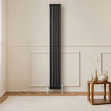 Radiateur à colonnes ovales noir, 1800 x 240 mm, installé contre un mur clair, avec un sol en bois et une table en bois à côté