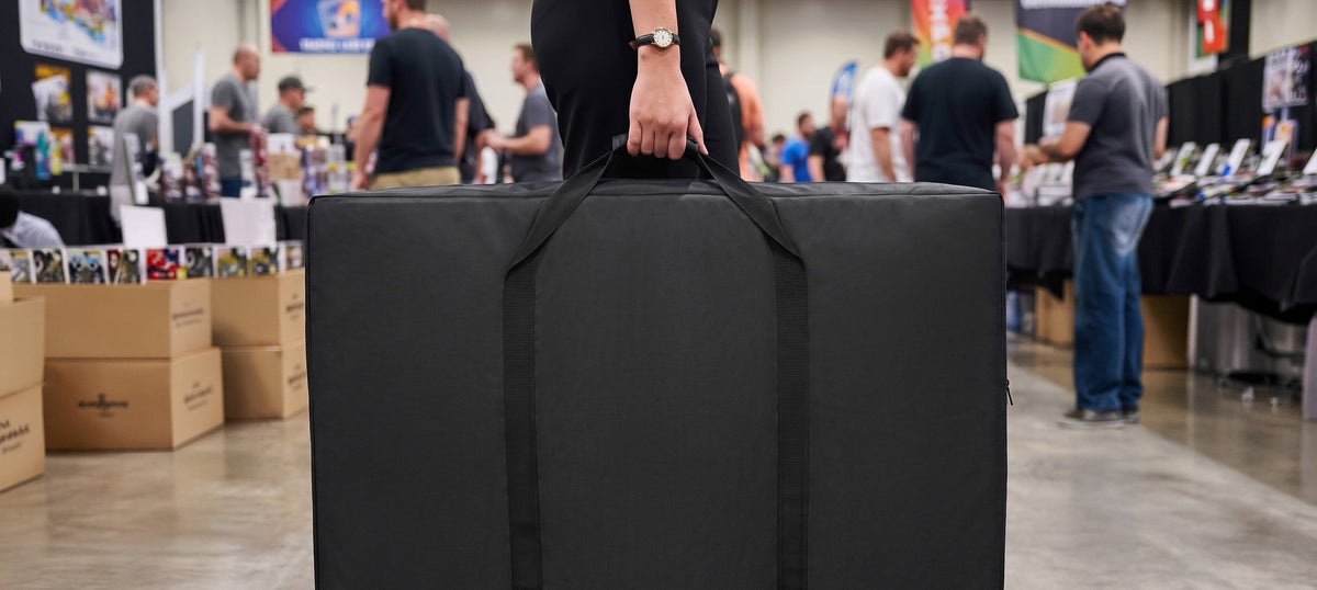 Grand sac noir avec des poignées solides, transporté par une personne, entouré de stands d'exposition et de visiteurs à un événement