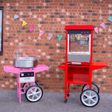 Machine à pop-corn rouge et machine à barbe à papa rose, toutes deux sur des chariots à roulettes, devant un mur en briques avec des fanions colorés