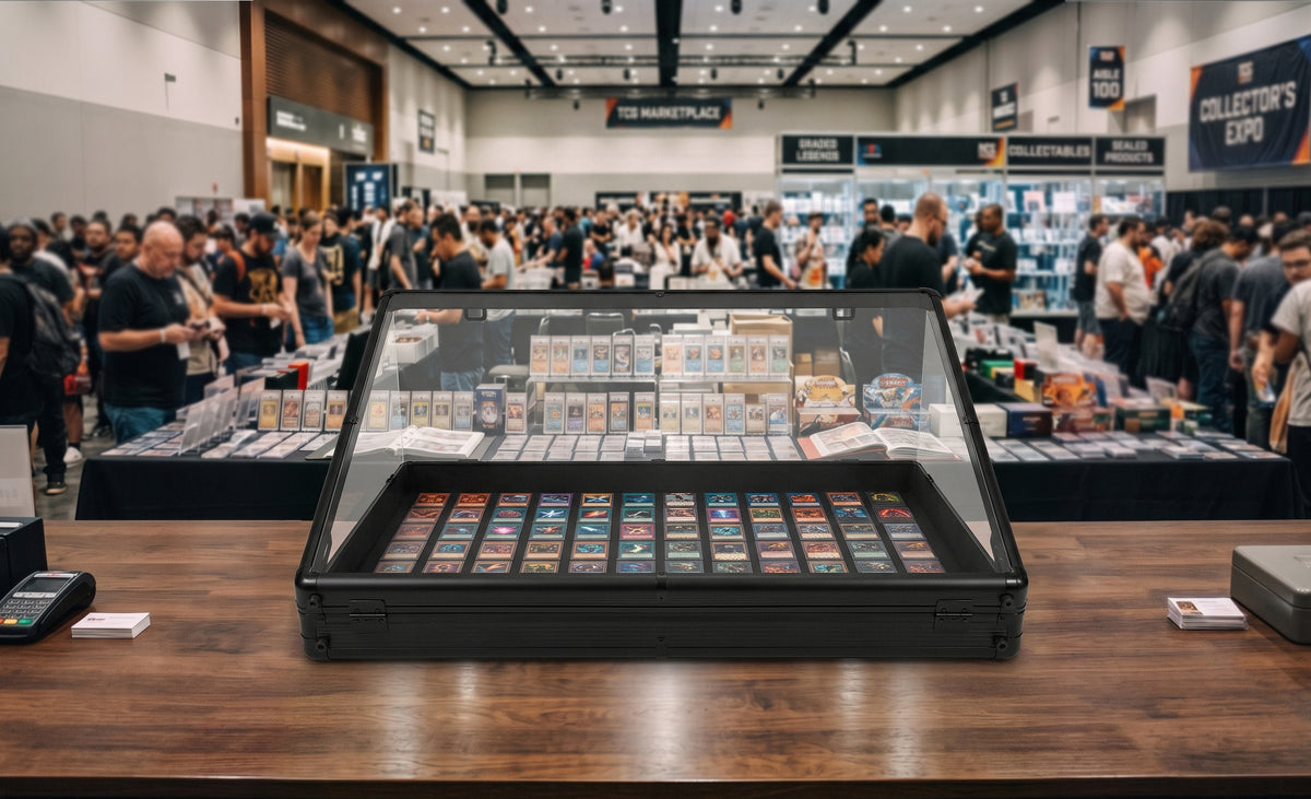 Vitrine en verre noire affichant des cartes de collection colorées sur une table en bois, avec une foule en arrière-plan lors d'un événement