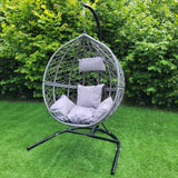 Chaise suspendue en rotin gris avec coussins moelleux, suspendue sur un support noir, entourée de verdure luxuriante